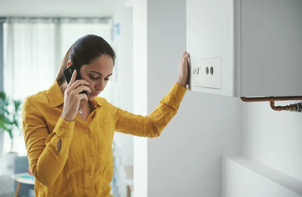 Broken Boiler Woman In A Yellow Blouse On The Phone Next To Her Boiler